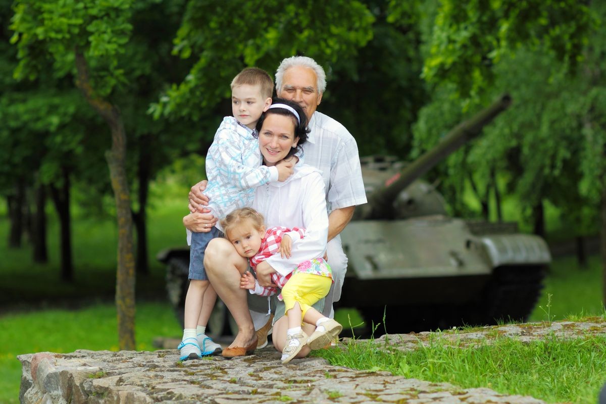 Romantic portrait of three generations of family on a background of vintage military tank